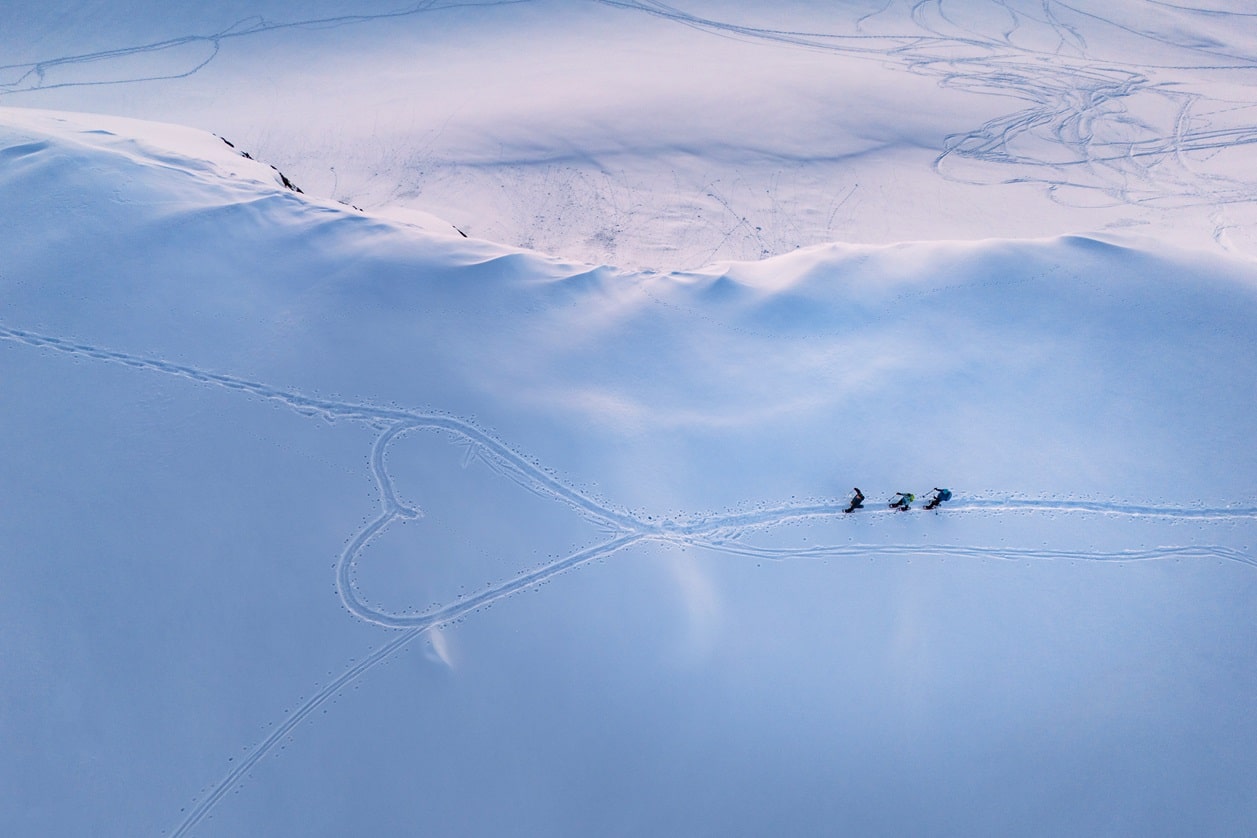 3 people walking with snowshoes through the snow, shaping a heart